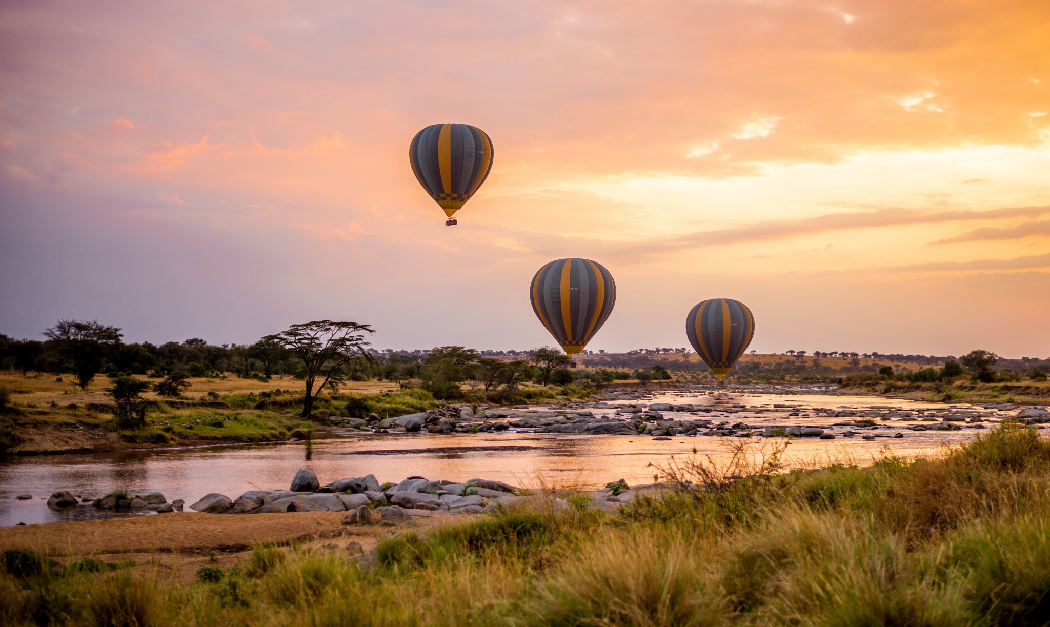 Three hot air balloons floating above the Serengeti at sunrise