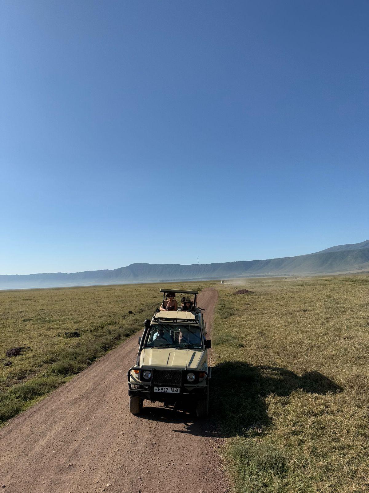 A safari vehicle carrying guests along a road across the Ngorongoro Crater floor