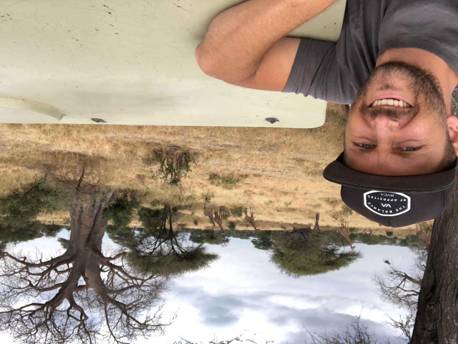 Reed Safari guest smiling during a game drive with giraffes in the background