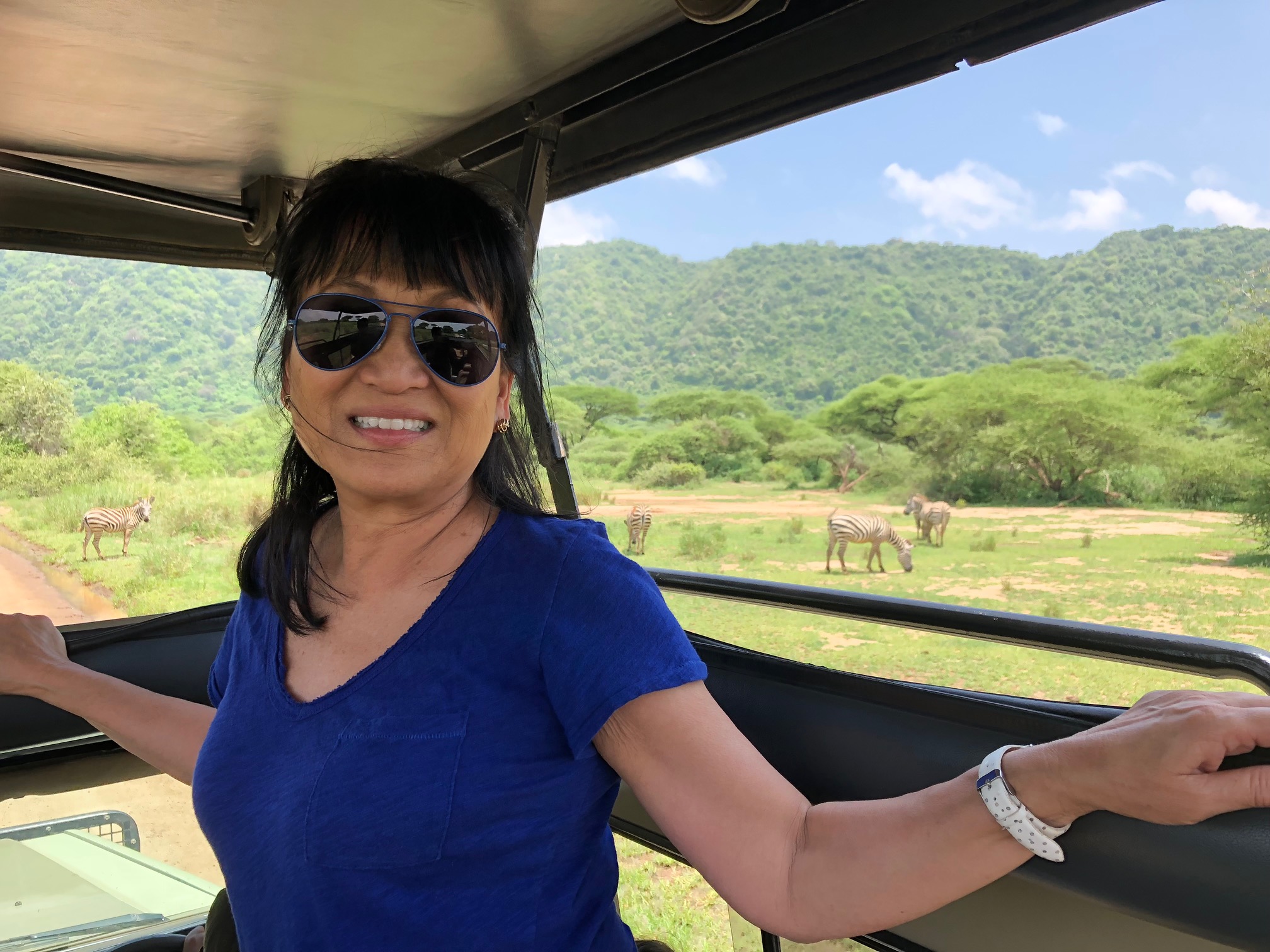 Guest smiling during a game drive as zebras graze nearby